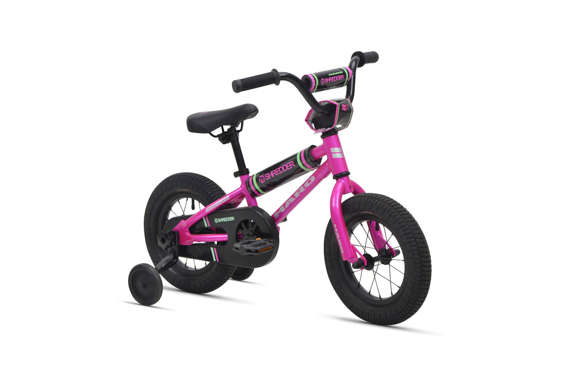 Shredder 12: small pink kids pedal bike with training wheels, black seat and handlebars on white background.