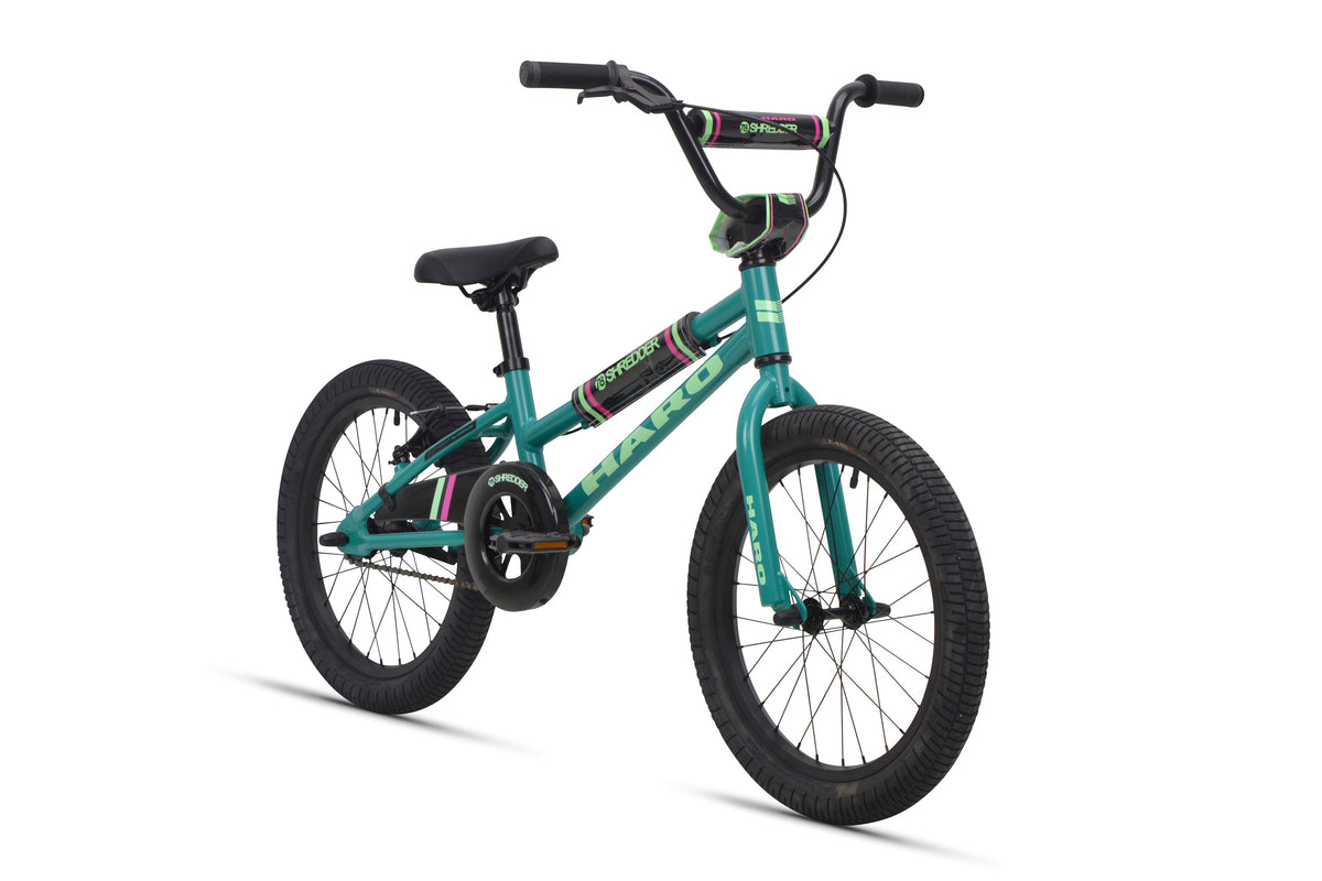 A teal Shredder 18 ST girls' bike with black tires, black seat, low top tube, green and purple accents; no training wheels.